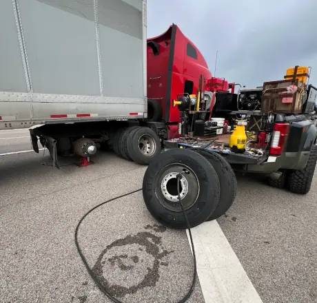 Breaux's Roadside service truck alongside a red semi tractor with a box trailer jacked up and the drive tire removed for replacement