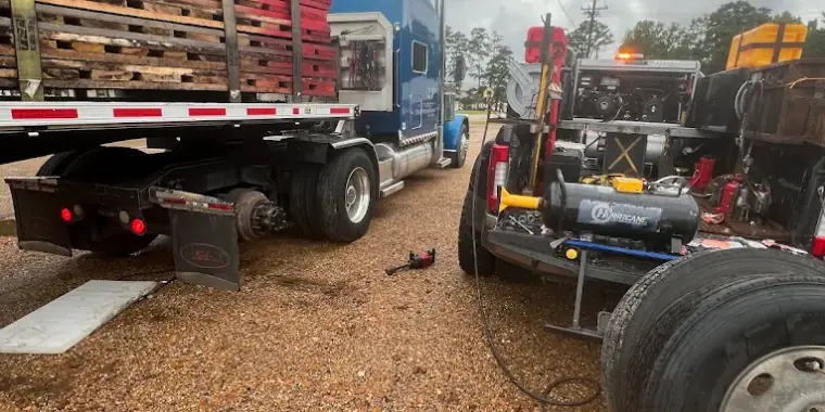 Breaux's Roadside service truck parked alongside a blue semi tractor hauling a flatbed load of pallets, with a replacement tire staged on the ground